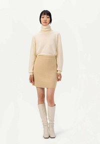 Krämfärgad polokrage och en beigefärgad ribbad kjol tillsammans med knähöga, off-white stövlar, som har en slät yta och en figurnära design.