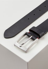 Black leather belt featuring a silver metal buckle, straight edges, and red stitching detail near the buckle. Textured leather surface.