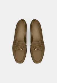 Mocassins en daim marron avec un détail de chaîne dorée sur le devant. Bout arrondi et semelle plate avec une doublure intérieure confortable.