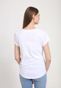 Camiseta blanca de manga corta con cuello redondo, textura suave y ajuste holgado, combinada con jeans de denim azul claro.