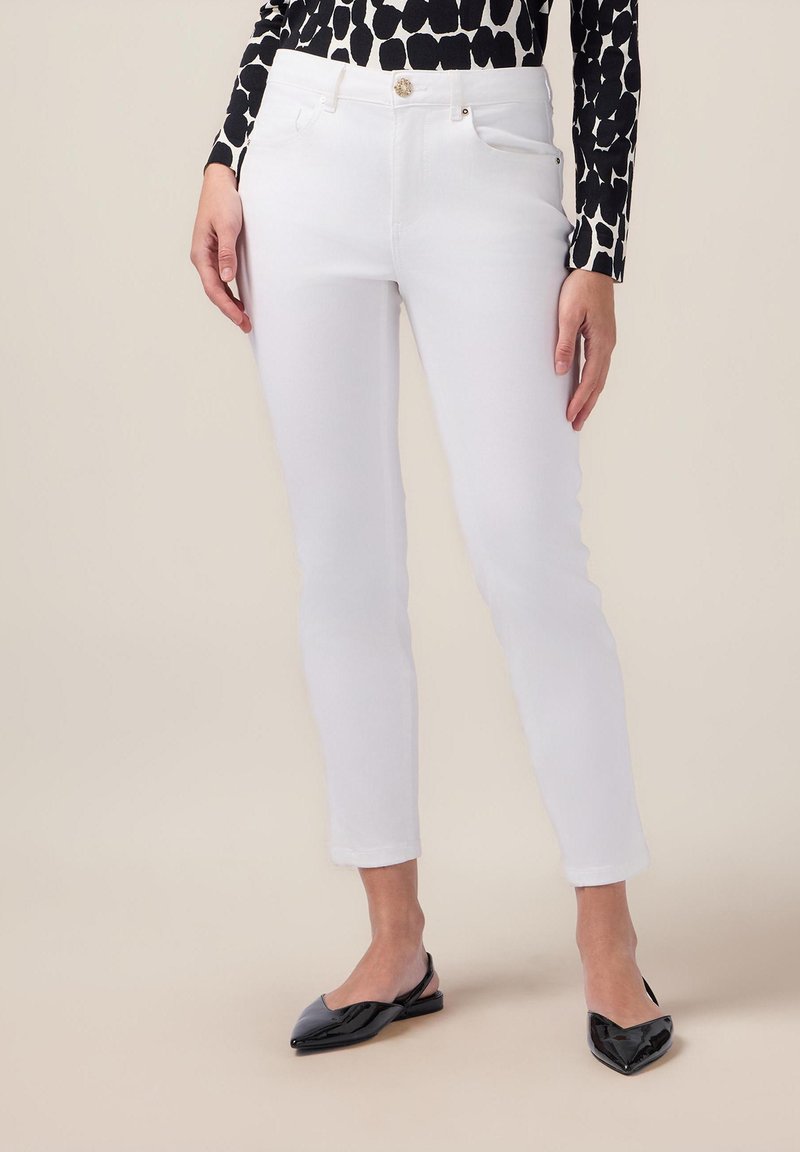 Vita jeans med en figurnära design och lätt stretch. Utrustad med framfickor, guldknappsdetalj och en kort längd. Kombineras med svarta ballerinaskor.