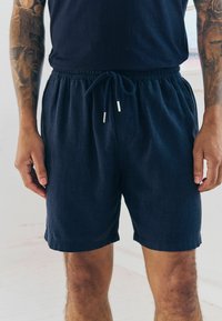 Shorts bleu marine en tissu doux avec une taille élastique et un cordon de serrage, arborant des embouts métalliques argentés sur le cordon.