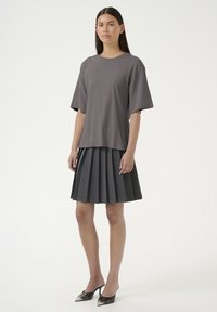Grå jersey t-shirt med afslappet pasform, parret med en plisseret mørkegrå nederdel og spidse sorte hæle med refleksfinish.
