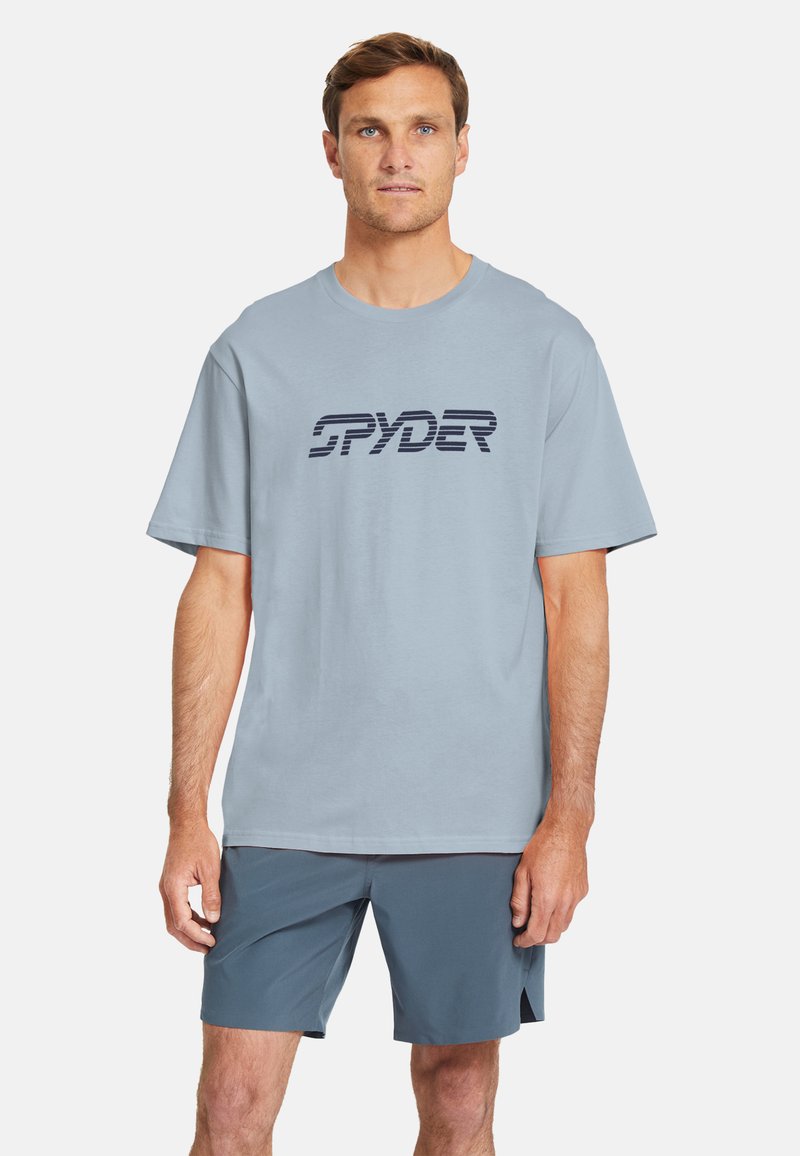 Camiseta de manga corta azul claro con un logo "SPYDER" en azul oscuro. Presenta un corte relajado y material de algodón suave, combinada con pantalones cortos oscuros.