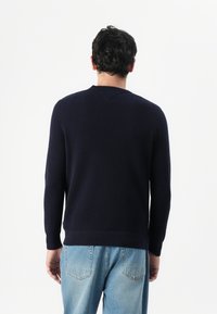 Granatowy sweter z dzianiny z długimi rękawami, okrągłym dekoltem i fakturowanym materiałem, zestawiony z jasnoniebieskimi dżinsami. Widoczne szwy na plecach.