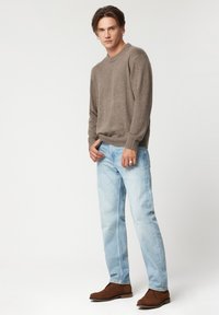 Brązowy sweter z dzianiny, jasnoniebieskie dżinsy, brązowe zamszowe botki za kostkę. Prosty i klasyczny design z prążkowanymi mankietami i luźnym krojem.