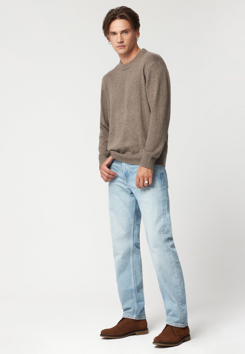 Brązowy sweter z dzianiny, jasnoniebieskie dżinsy, brązowe zamszowe botki za kostkę. Prosty i klasyczny design z prążkowanymi mankietami i luźnym krojem.
