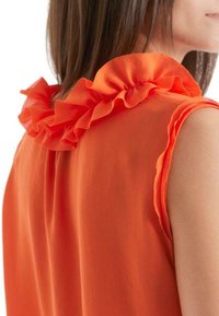 Top sin mangas naranja con un escote acampanado, textura suave y un ligero brillo, con un corte relajado y costuras de hombro redondeadas.