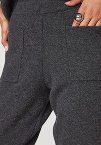 Pantaloni grigio scuro realizzati in un morbido tessuto testurizzato, dotati di ampie tasche a toppa e vita aderente. Design minimalista con linee pulite.