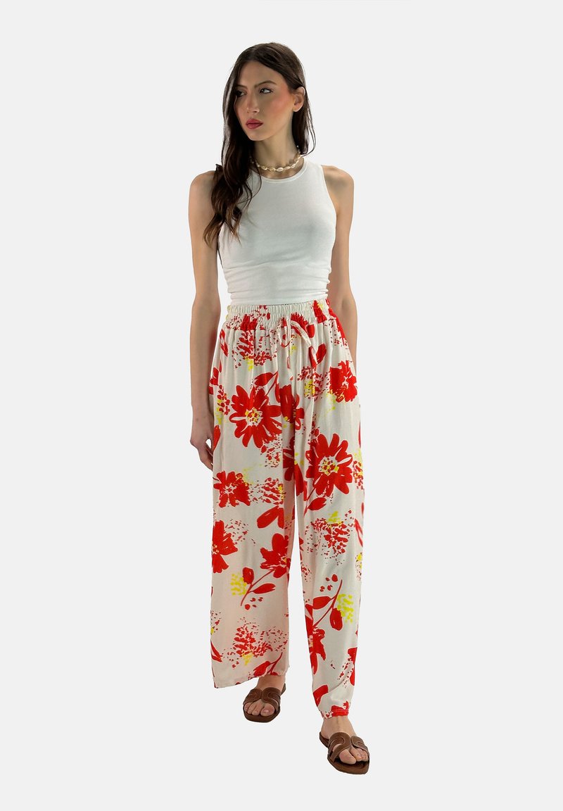 Bloemrijke, wijde broek in het wit met rode en gele bloemenpatronen; elastische tailleband; lichtgewicht stof, gecombineerd met een witte tanktop.