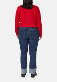 Czerwony top z długim rękawem zestawiony z dżinsami. Dżinsy mają podwinięte mankiety, dwie tylne kieszenie oraz prosty krój nogawek.
