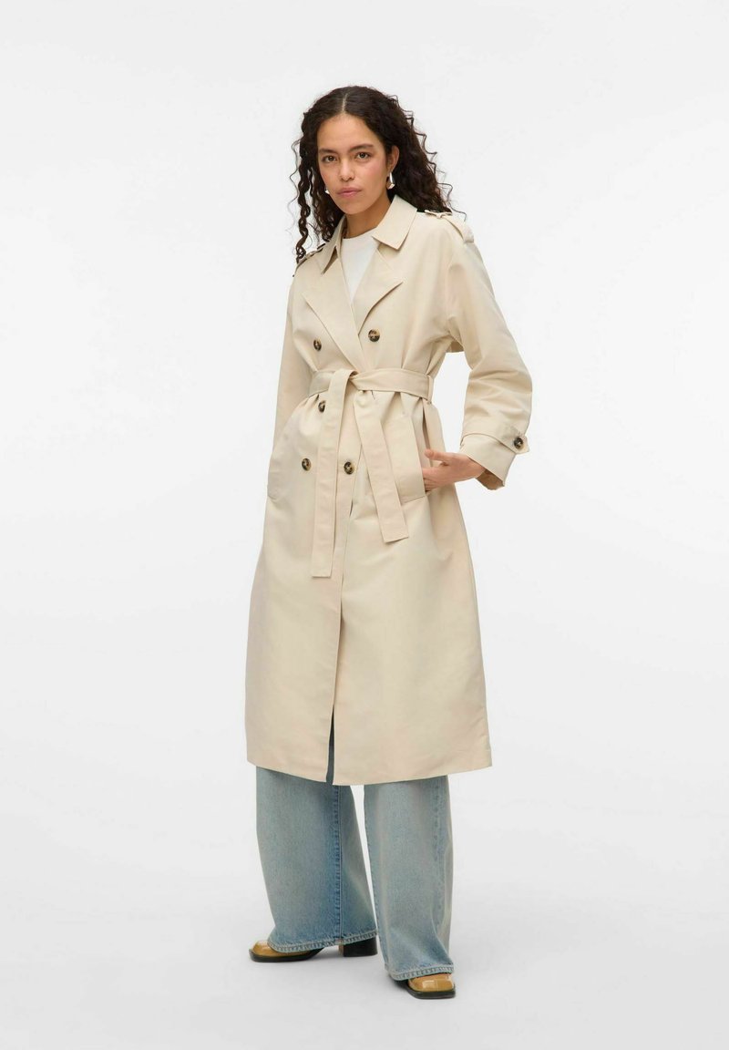 Beige trenchcoat med dubbelknäppt framtill, knytmidja och två framfickor. Lätt tyg med rak passform, kombinerat med vida jeans.