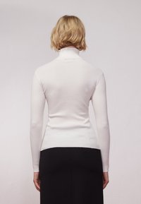 Biały, prążkowany sweter z golfem i długimi rękawami, o dopasowanym kroju. W połączeniu z ciemną spódnicą, ukazującą kontrastową paletę kolorów.