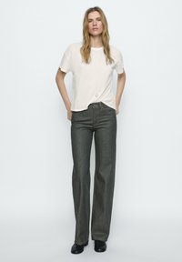 Lichtbeige t-shirt met korte mouwen en een losse pasvorm, gecombineerd met donkergrijze hoge taille wijde jeans. Zwarte schoenen maken de outfit compleet.