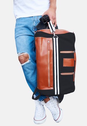 Black and brown duffel bag made of leather and fabric, featuring two front zip pockets, white stripe accents, and a sturdy shoulder strap.