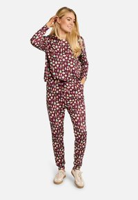 Dviejų dalių laisvalaikio aprangos komplektas tamsiai violetinės spalvos su šventine ornamentų, lankų ir medžių spauda. Komplekte yra elastinė juosmens juosta ir užsegami kelnių apačios.