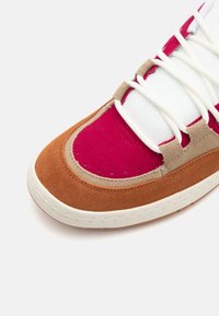 Sneaker med et flerfarvet design med brun ruskind, lyserød ruskind, hvid mesh og lyse beige akcenter. Hvide snørebånd og tekstureret såldetalje.