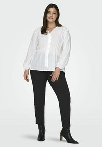 Vitt, knäppt blus med texturerad tyg, avslappnad passform, lätt insydd midja, långa ärmar. Kombineras med svarta smala byxor och ankelstövlar.