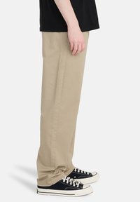 Beige bomuldsbukser med lige pasform, der har sidesømme og en subtil tekstur. Kombineret med sorte lave sneakers.