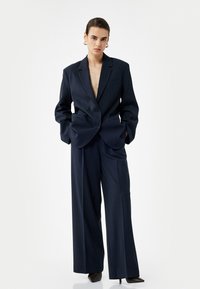 Marineblå stribede jakkesæt med en blazer med bred revers og højtsiddende, vide bukser. Materialet har en glat tekstur.