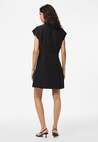 Vestido preto sem mangas com corpete ajustado, saia rodada e pregas laterais; textura suave e design até ao joelho; combinado com sandálias de salto pretas.