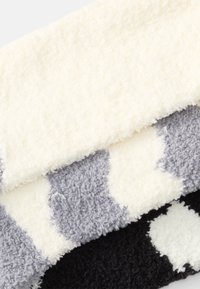Drei überlappende, strukturierte Decken: cremefarben, grau mit weißen Punkten und schwarz mit weißen Dots. Weicher, flauschiger Stoff mit unterschiedlichen Farbmustern.