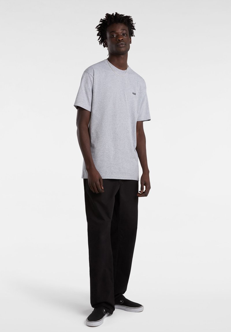 Camiseta gris de manga corta con cuello redondo y pequeño logo, combinada con pantalones sueltos negros y zapatillas negras. Diseño simple y clásico.