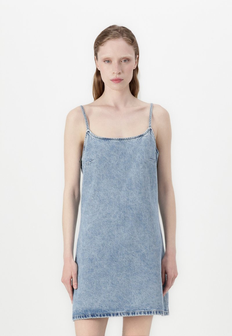 Traper haljina u svijetlo plavoj boji s tankim podešivim trakama, kvadratnim izrezom i bočnim džepovima. Ima ravni kroj i razderanu rub.