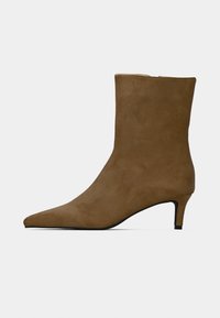 Bottine en daim marron avec bout pointu et talon bas arrondi. Texture lisse avec un design sans coutures et des détails de couture subtils.