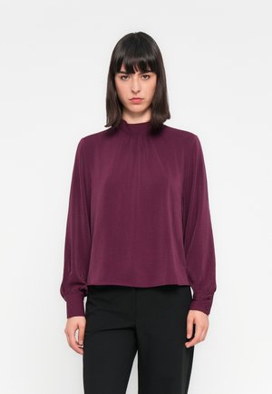 Burgundy long-sleeve blouse with a high neckline, gathered detail, and buttoned cuffs, paired with black trousers. Smooth texture.