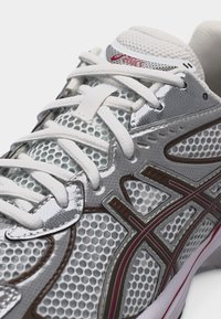 Λευκό και ασημί παπούτσι για τρέξιμο με λευκά κορδόνια, επάνω μέρος από πλέγμα και κόκκινο λογότυπο Asics στη γλώσσα και στην πλευρά.