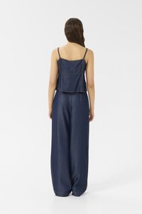 Mono vaquero con un top corto ajustado y pantalones de pierna ancha, con tirantes finos, de color azul oscuro y con costuras visibles destacadas.