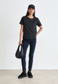 Black short-sleeve T-shirt, blue skinny jeans, black platform sneakers, and a black handbag. Simple, casual design with smooth textures.
