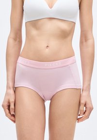 Ohlapen bombažni spodnji del svetlo roza barve z mehkim elastičnim pasom, na katerem je napis "PIECES" v belih črkah. Enostavna, gladka zasnova brez vzorcev.