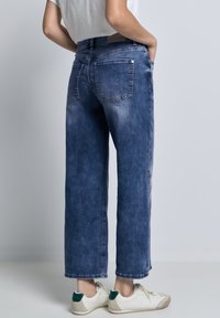 Donkerblauwe denim jeans met een relaxed fit, voorzien van achterzakken en een soepele textuur. Gestyled met witte sneakers en een lichte top.