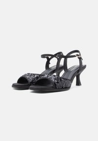 Black heeled sandals with open toe, featuring a textured black sequined design on the strap, adjustable ankle strap, and a slim heel.