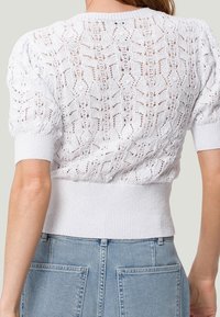Suéter blanco de punto con intrincados patrones similares a encaje, mangas cortas abullonadas y cinturilla acanalada. Acabado texturizado con material ligero.