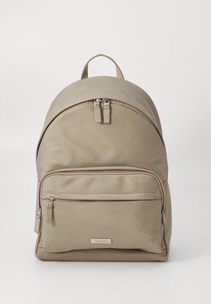 Beige Rucksack aus Stoff mit abgerundetem Deckel, zwei Reißverschlussfächern und einer Vordertasche. Verfügt über einen runden Griff und ein Logo-Detail.