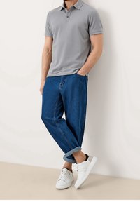 Polo gris avec un col, associé à un jean bleu à coupe décontractée et des baskets blanches. Texture lisse, design décontracté et manches retroussées.