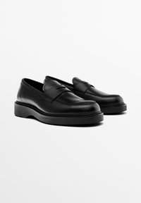 Pair of black leather penny loafers with thick rubber soles on a white background, angled right.
