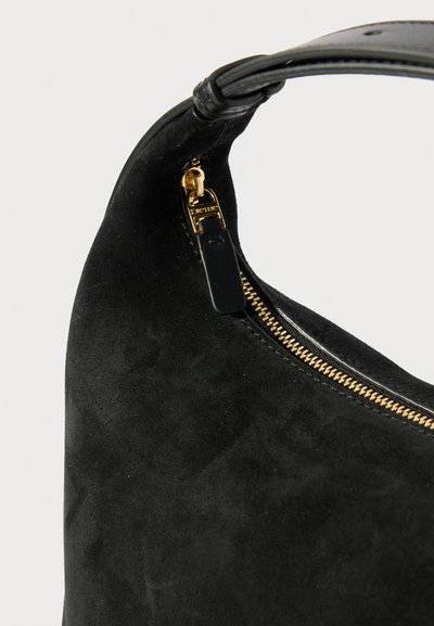 Zwarte suède handtas met een gladde textuur, voorzien van een gouden metalen rits en een gevlochten handvat, met een gebogen ontwerp.