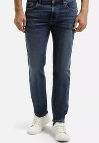 Granatowe dżinsy o prostym kroju, z przednimi kieszeniami, zamkiem błyskawicznym i minimalnym przetarciem. Połączone z białymi sneakersami.