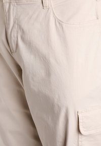 Beige cargo kalhoty s hladkým povrchem, vybavené boční kapsou a standardními předními kapsami, šitými švy a uvolněným střihem.