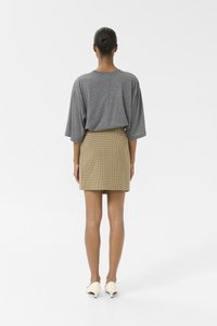 Chemise oversize grise et mini-jupe à carreaux jaunes, associées à des talons crème. Tissu lisse avec un design simple et moderne.