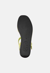 Sandal con suola nera che mostra la taglia 38 e una grande "C," con cinturini verde chiaro visibili di lato su uno sfondo bianco.
