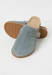 Suede clogs in soft blue, featuring a buckle strap and brown rubber sole with vertical grooves for traction. Smooth inner lining.