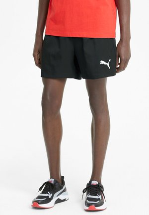 Black shorts with a loose fit, featuring a white Puma logo. Paired with black, white, and red athletic shoes with a textured design.