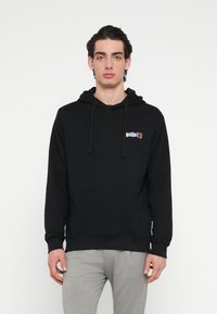 Svart huvtröja med framficka, med en flervägssfärgad logotyp på bröstet. Mjukt tyg, normal passform och ribbade muddarna.