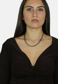 Zilveren ketting rust op een donker, V-hals top, met een gedraaide vormgeving en een gladde textuur, wat een strakke en moderne esthetiek benadrukt.