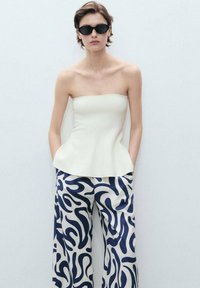 Strapless cream peplum top paired with wide-leg pants featuring a navy blue abstract pattern. Smooth, lightweight fabric with a structured design.